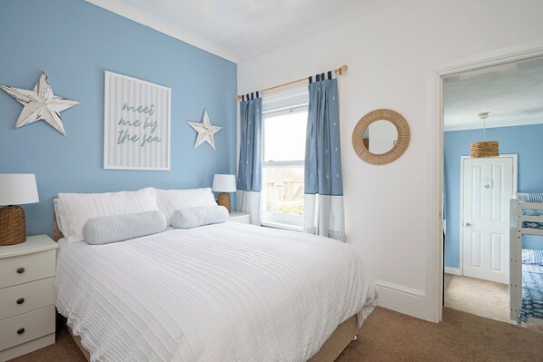 A bedroom with a bed, two nightstands, a window with curtains, a star decoration, a wall art with text, and a door leading to another room.
