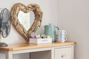 A wooden desk with a heart-shaped mirror, a kettle, a box of Clipper tea, and a mug with fish designs.