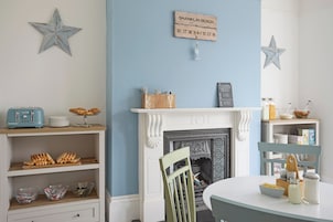 Un coin repas agrémenté d’une cheminée blanche, d’une décoration en forme d’étoile et d’un panneau indiquant les coordonnées de la plage de Shanklin.