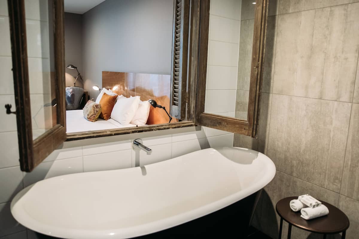 Une salle de bain moderne avec une baignoire sur pieds, un grand miroir et un petit tabouret sur lequel sont posées des serviettes.