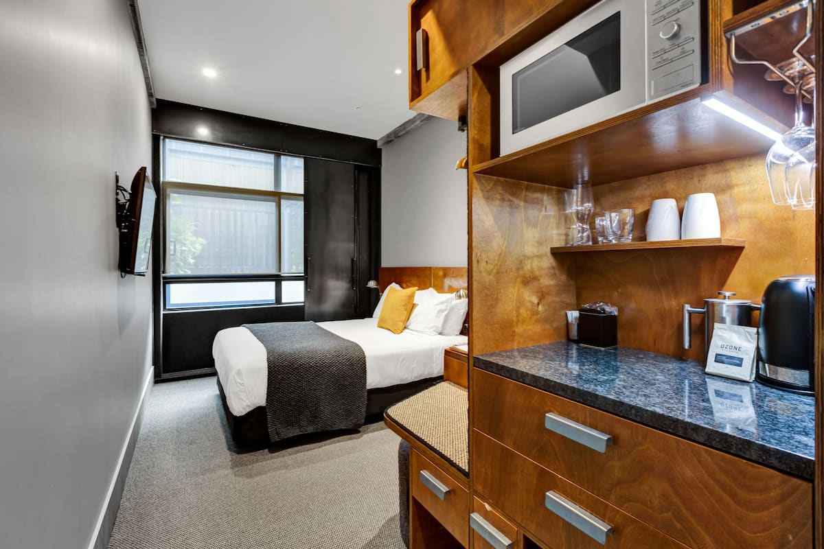 Une chambre d’hôtel moderne équipée d’un lit, d’un meuble en bois contenant un four à micro-ondes et une machine à café, ainsi que d’une fenêtre donnant sur un paysage agréable.