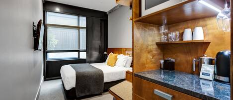 Una habitación de hotel moderna con una cama, un mueble de madera con microondas, una cafetera y una ventana con vistas.