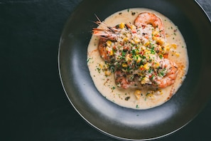 A plate of shrimp with a creamy sauce and corn on a dark background.
