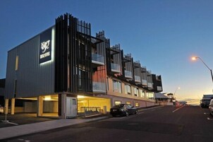 Un hotel moderno con un logotipo destacado en la fachada, varios balcones y una entrada bien iluminada.