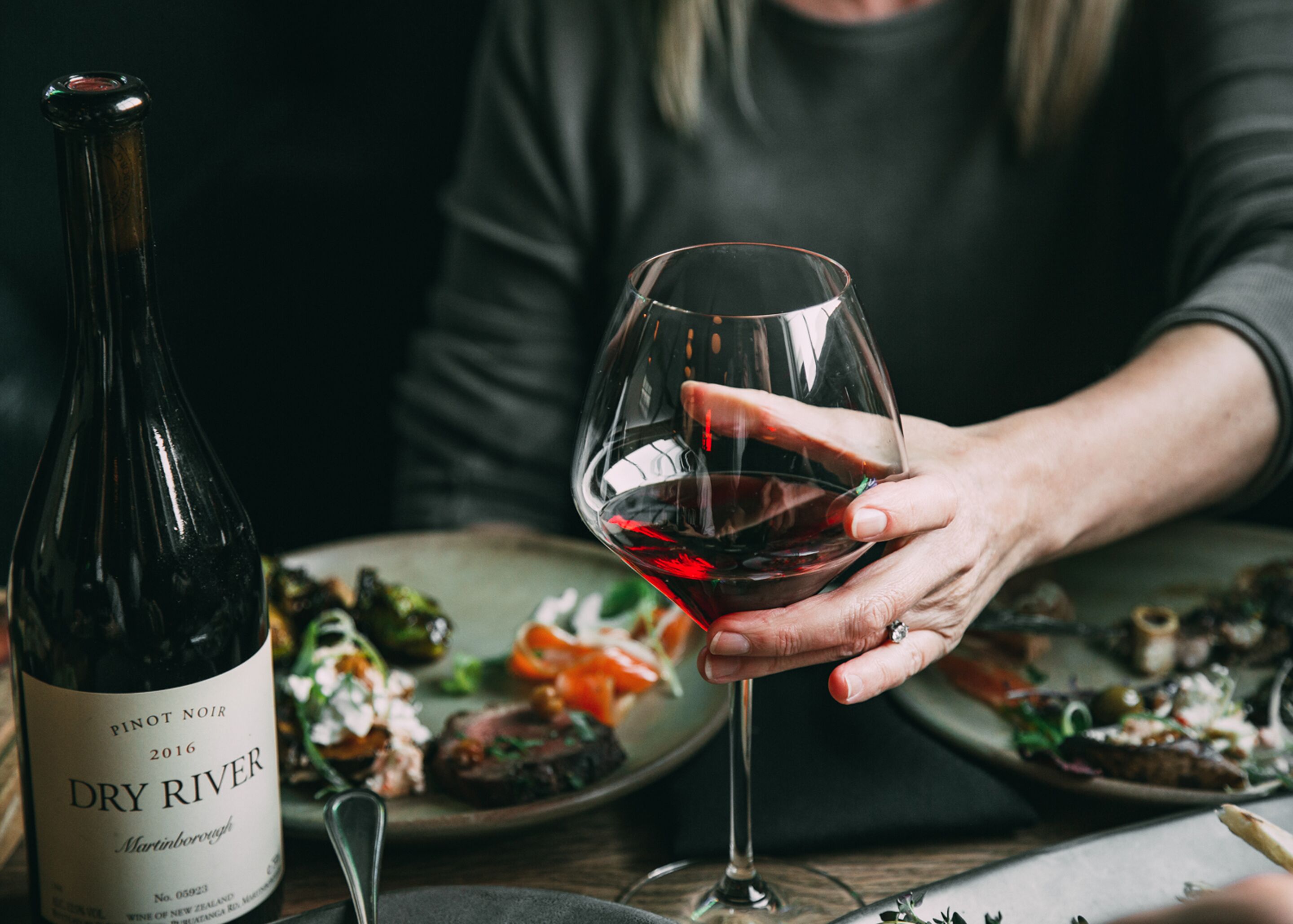 Eine Flasche Pinot Noir und ein Glas Rotwein auf einem Tisch mit einer Speiseplatte.
