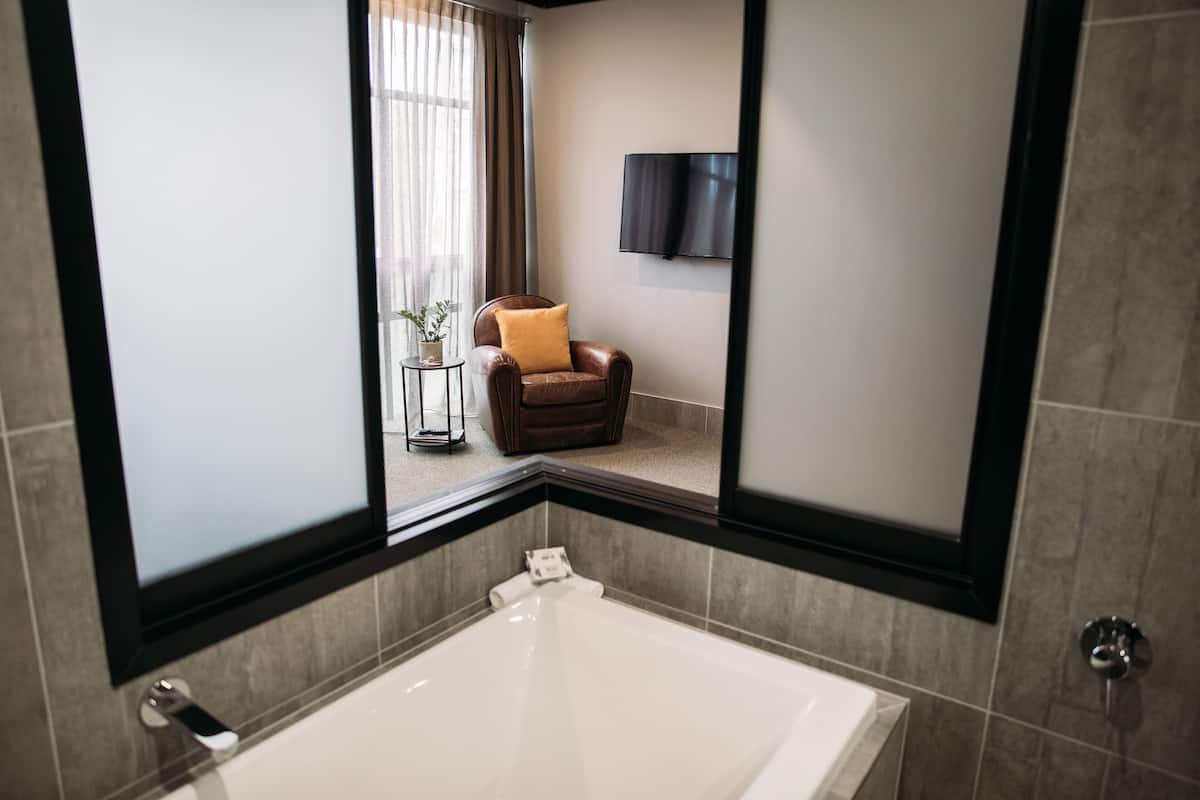 Une salle de bain moderne avec une grande baignoire, un fauteuil avec un coussin, une petite table avec une plante et un téléviseur à écran plat fixé au mur.
