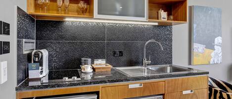 Una cocina moderna con un salpicadero de azulejos negros, electrodomésticos de acero inoxidable, armarios de madera y un lavamanos integrado.
