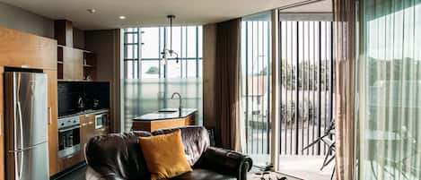 Et moderne køkken med stålemmer, en lædersofa og et spiseområde med udsigt gennem store vinduer.