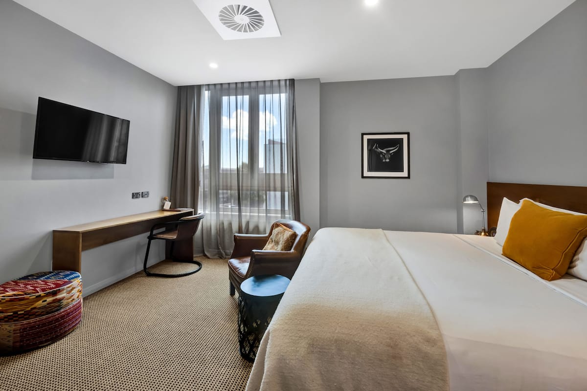 Une chambre d’hôtel moderne équipée d’un grand lit, d’un bureau, d’une chaise, d’une télévision et d’une fenêtre avec des rideaux.
