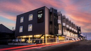 Un hotel moderno con un letrero llamativo, una zona de estacionamiento cubierta y vistas a la calle con vehículos en movimiento.