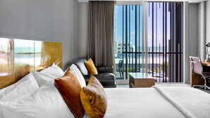 Una habitación de hotel moderna con una cama grande, un escritorio y un balcón con vistas a la ciudad.