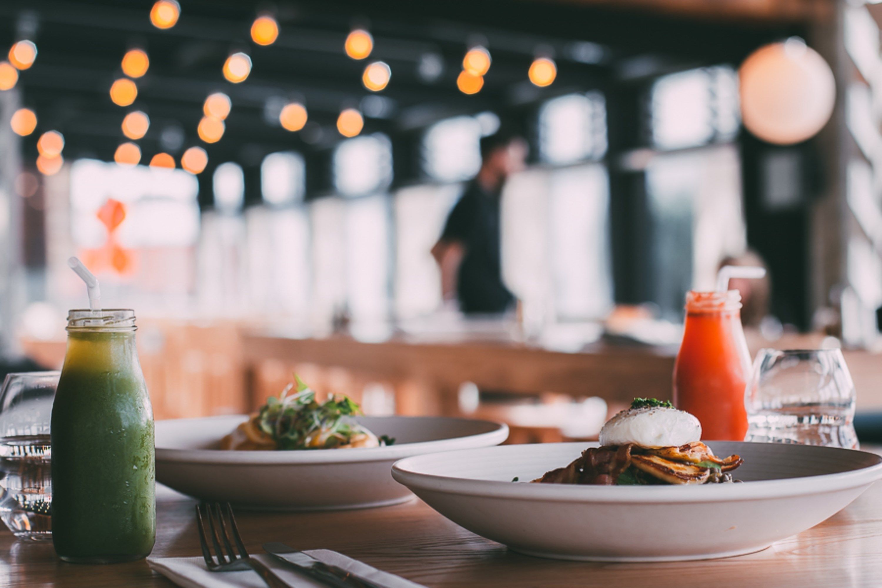 A restaurant setting with a table set for a meal, including plates of food, a green drink, and a red sauce bottle.