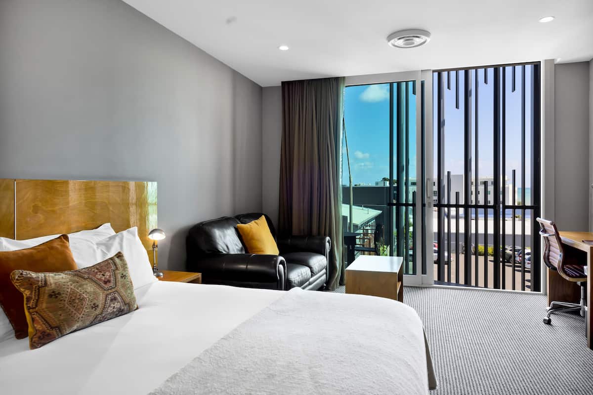 Une chambre d’hôtel moderne dotée d’un grand lit, d’un canapé en cuir, d’un bureau et d’un balcon offrant une vue sur la ville.