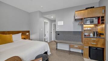 A hotel room with a large bed, a small desk, a microwave, and a refrigerator.