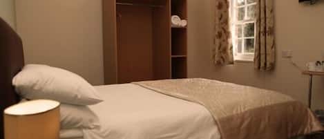 Une chambre à coucher comprenant un lit, une lampe de chevet, une armoire, une fenêtre avec des rideaux et un téléviseur à écran plat fixé au mur.