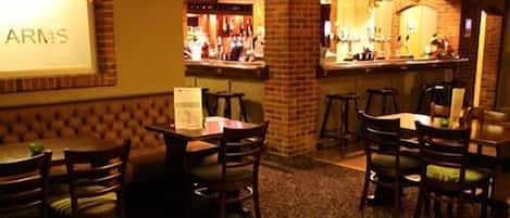 A bar area with a brick pillar, multiple tables and chairs, and a projection screen displaying "ARMS".