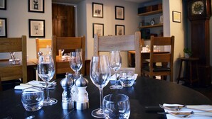Una mesa de comedor dispuesta con copas de vino y cubiertos, rodeada de sillas de madera.