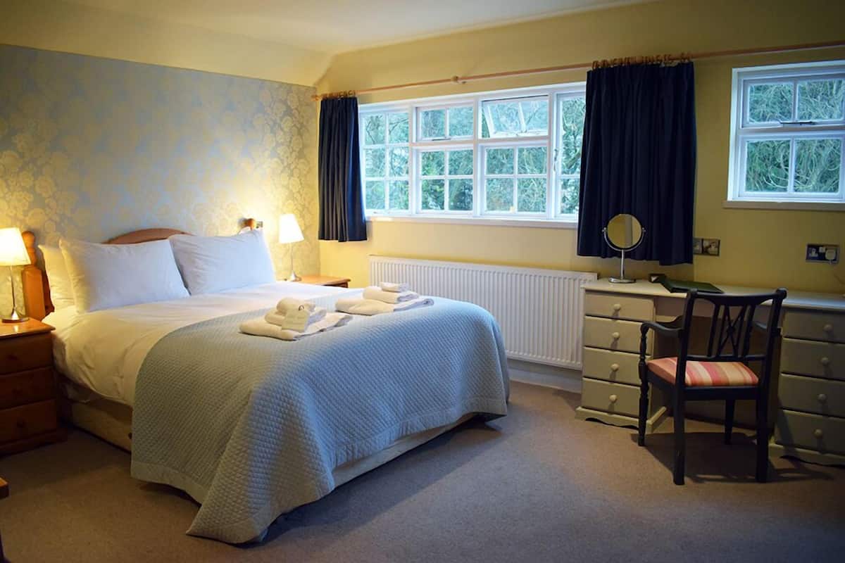 A bedroom with a bed, bedside tables, a dresser, a chair, and a window with curtains.