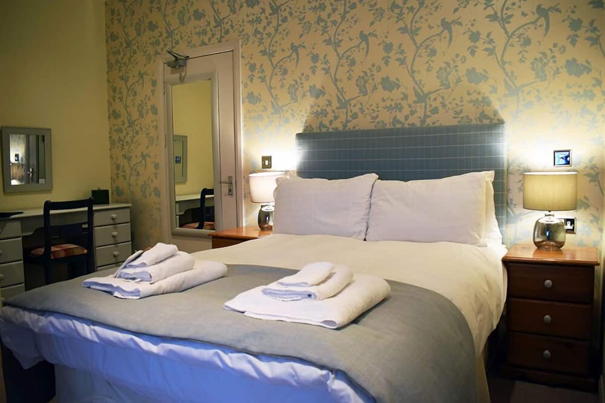 A neatly made bed with folded towels, a bedside table with a lamp, and a chair.