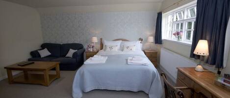 Habitación de hotel con cama, sofá, escritorio y ventana con cortinas.