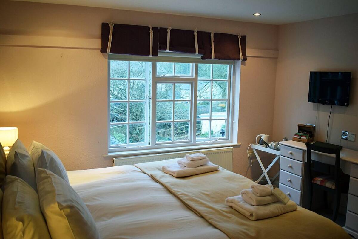 A hotel room with a large bed, a window with curtains, a bedside table with a lamp, and a TV mounted on the wall.