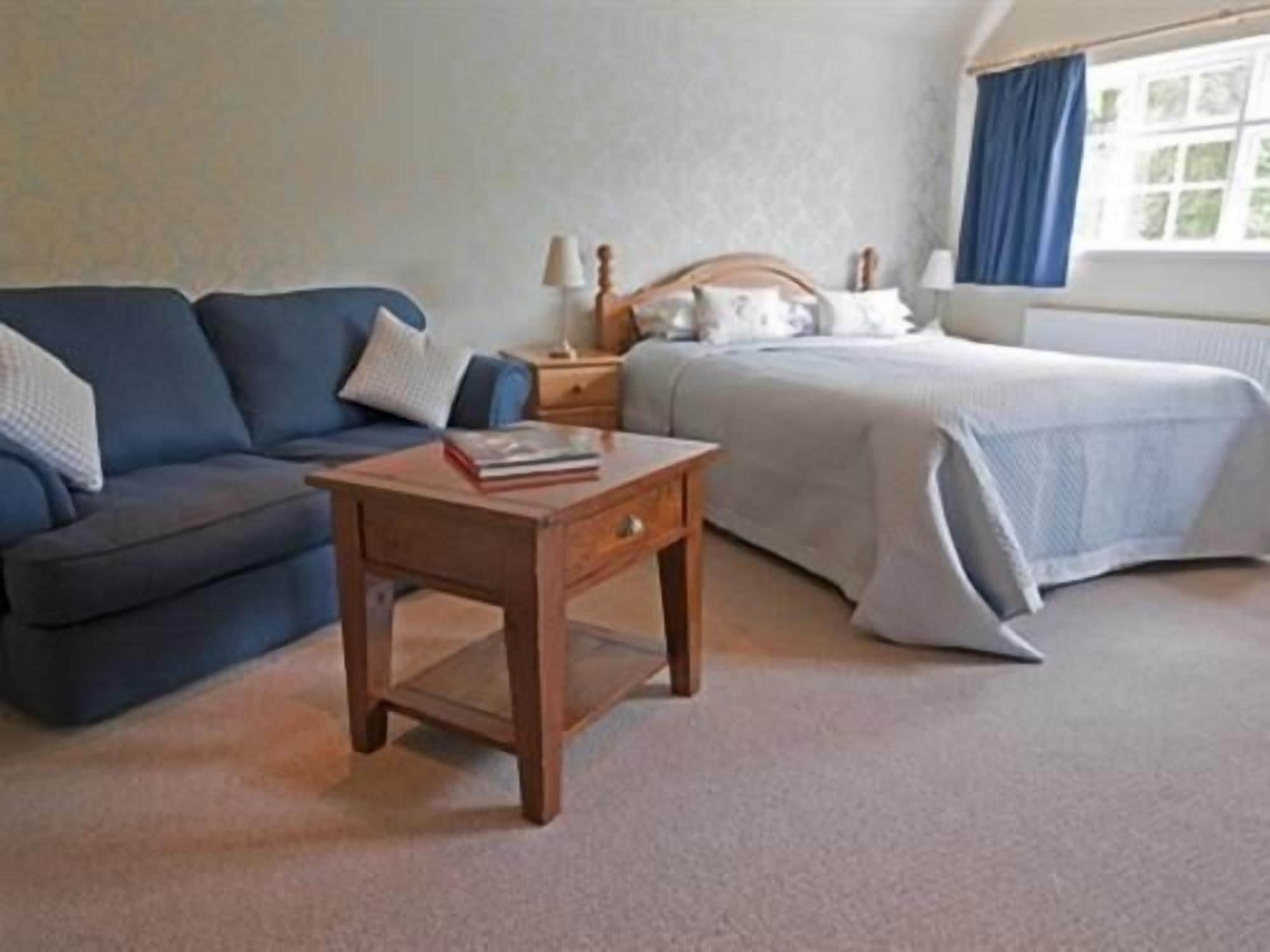A bedroom with a bed, a sofa, a nightstand, and a small table with a book.