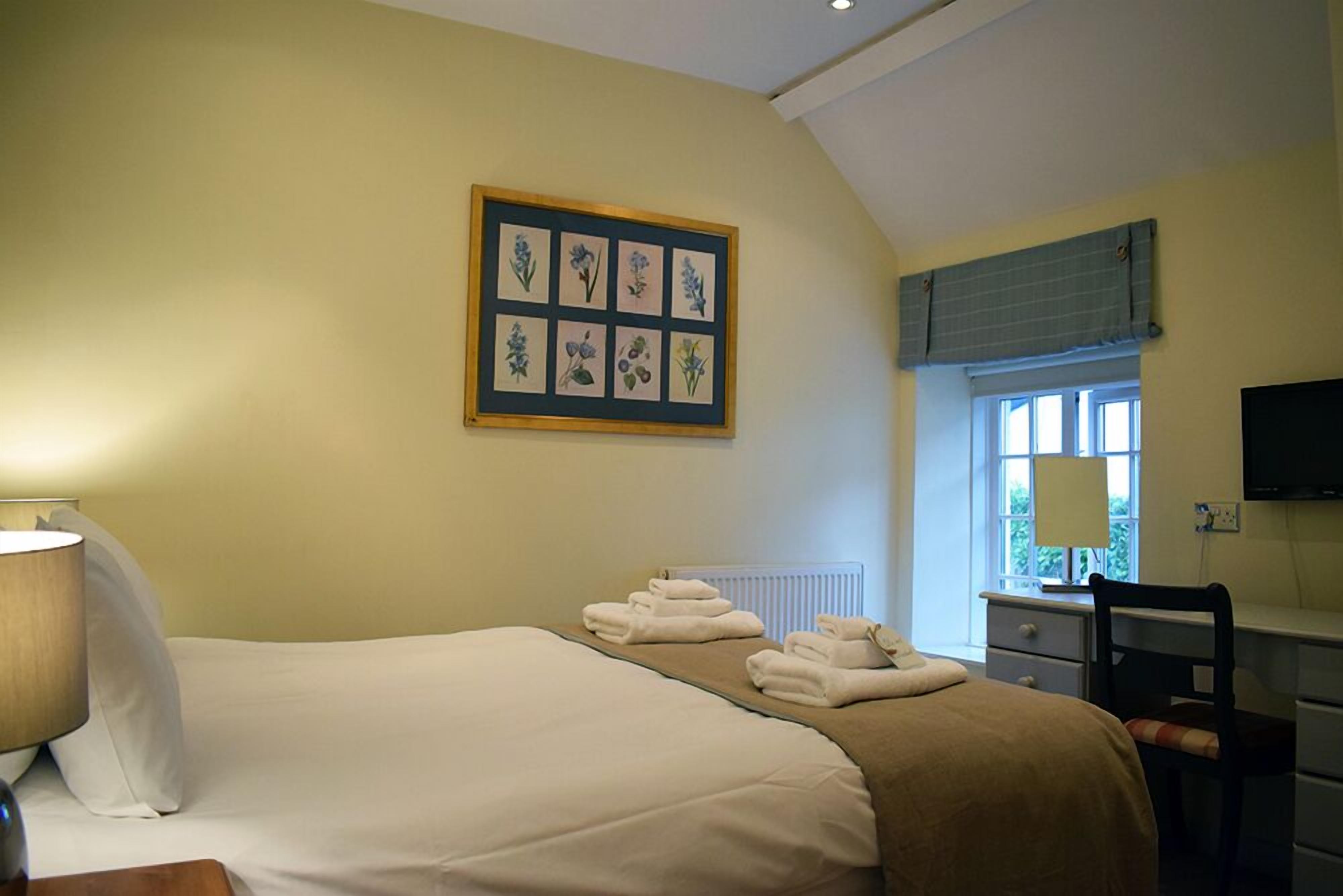 Une chambre d’hôtel comprenant un lit, un bureau avec une chaise, une fenêtre avec des stores et un téléviseur fixé au mur.