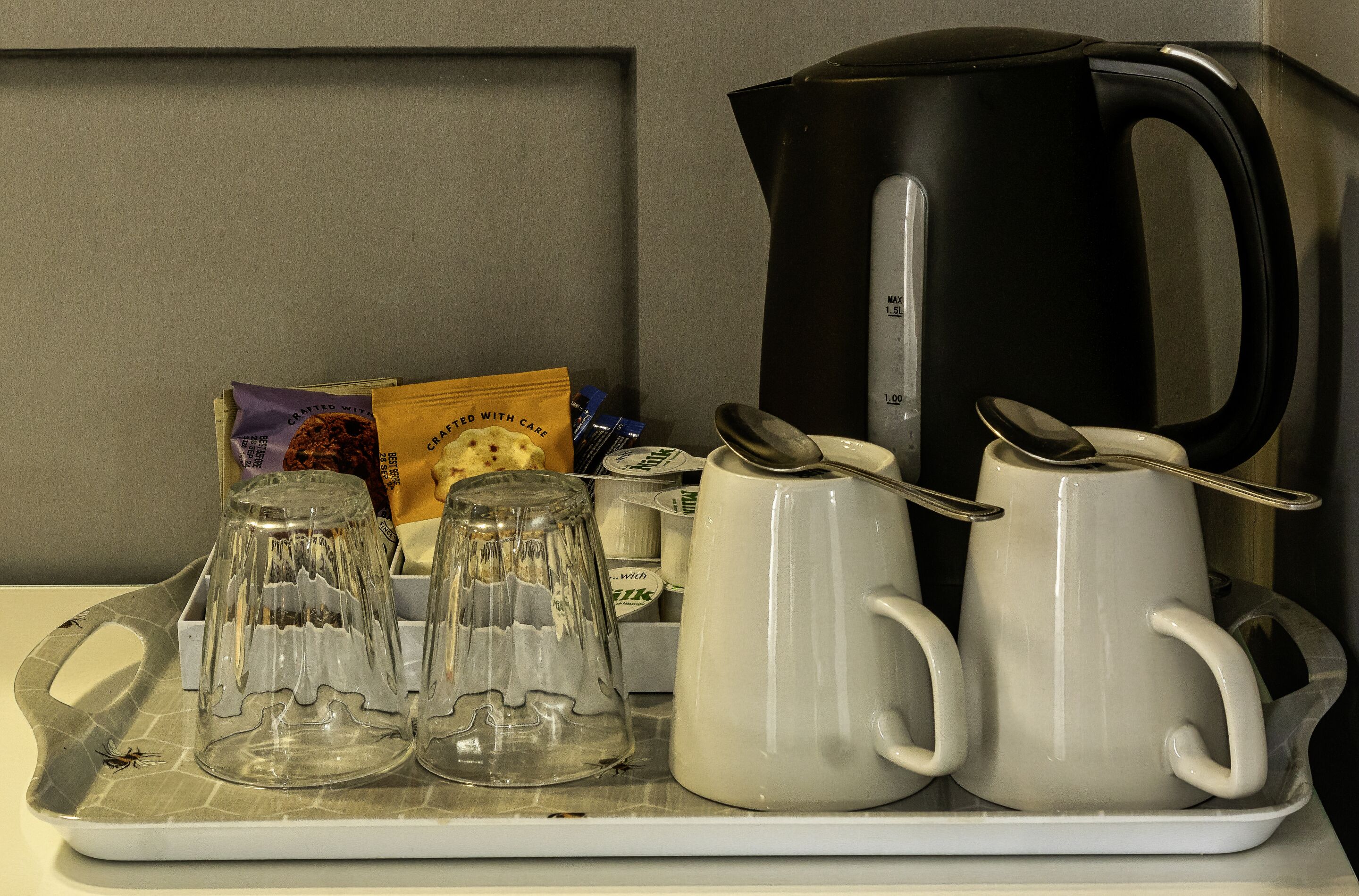 A tray with a coffee maker, two mugs, two glass carafes, a packet of cookies, and a box of tea.
