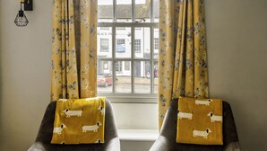 Two armchairs with a mustard-colored throw, positioned in front of a window with floral curtains. - The Green Dragon at Bedale by OYO (Bedale)