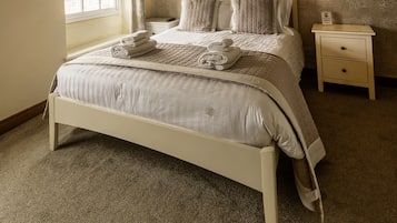 Una cama bien hecha con una colcha acolchada y almohadas, una mesita de noche con una lámpara y una ventana con cortinas.
