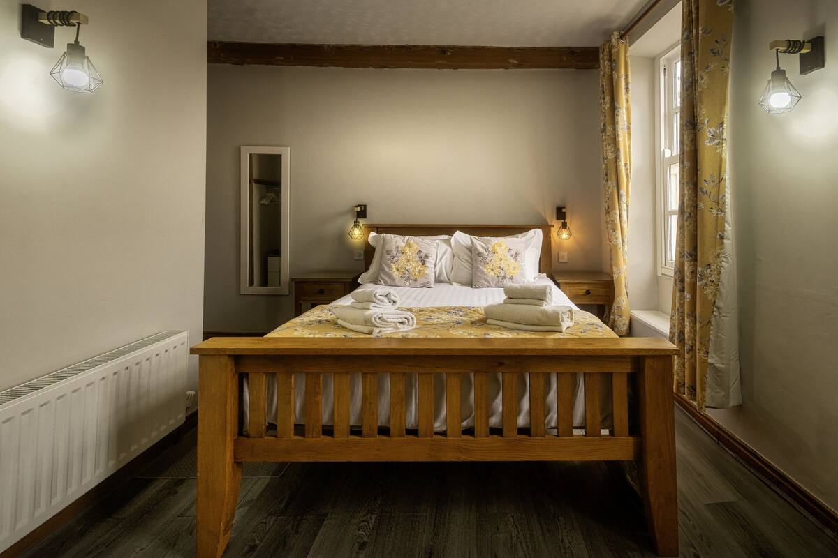 A wooden bed with a headboard, a bedside table, a mirror, and two wall-mounted lights.