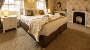 A bedroom with a large bed, bedside tables, a lamp, a fireplace, and a window with curtains. - The Green Dragon at Bedale by OYO (Bedale)