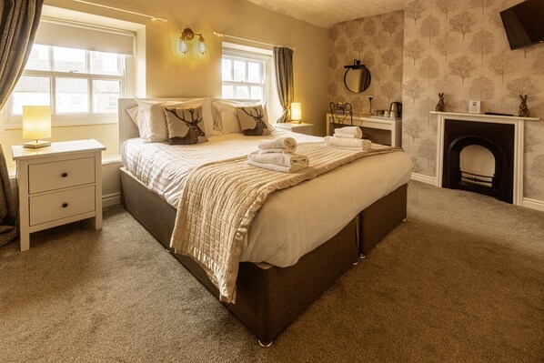 A bedroom with a large bed, bedside tables, a lamp, a fireplace, and a window with curtains.