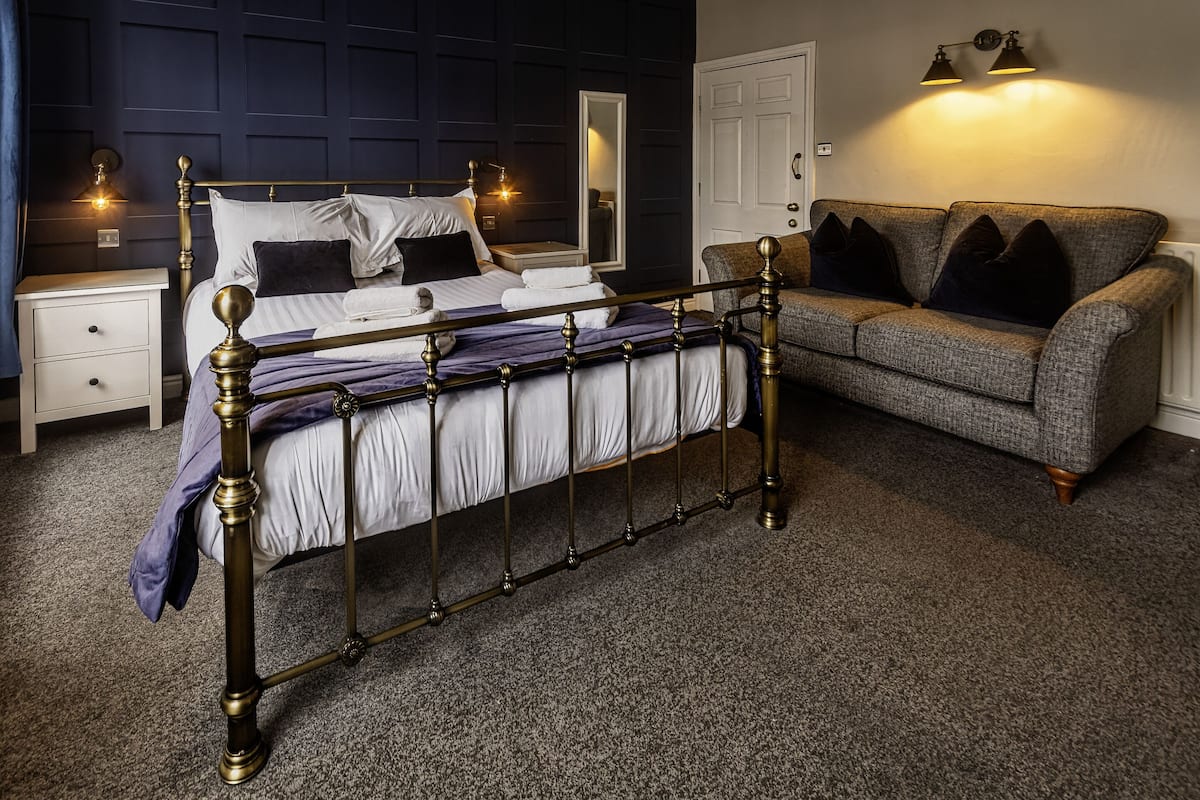 A bedroom with a bed, a nightstand, a dresser, a grey sofa, and a mirror.