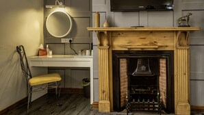 A room with a fireplace, a mounted TV, a desk with a chair, and a round mirror. - The Green Dragon at Bedale by OYO (Bedale)