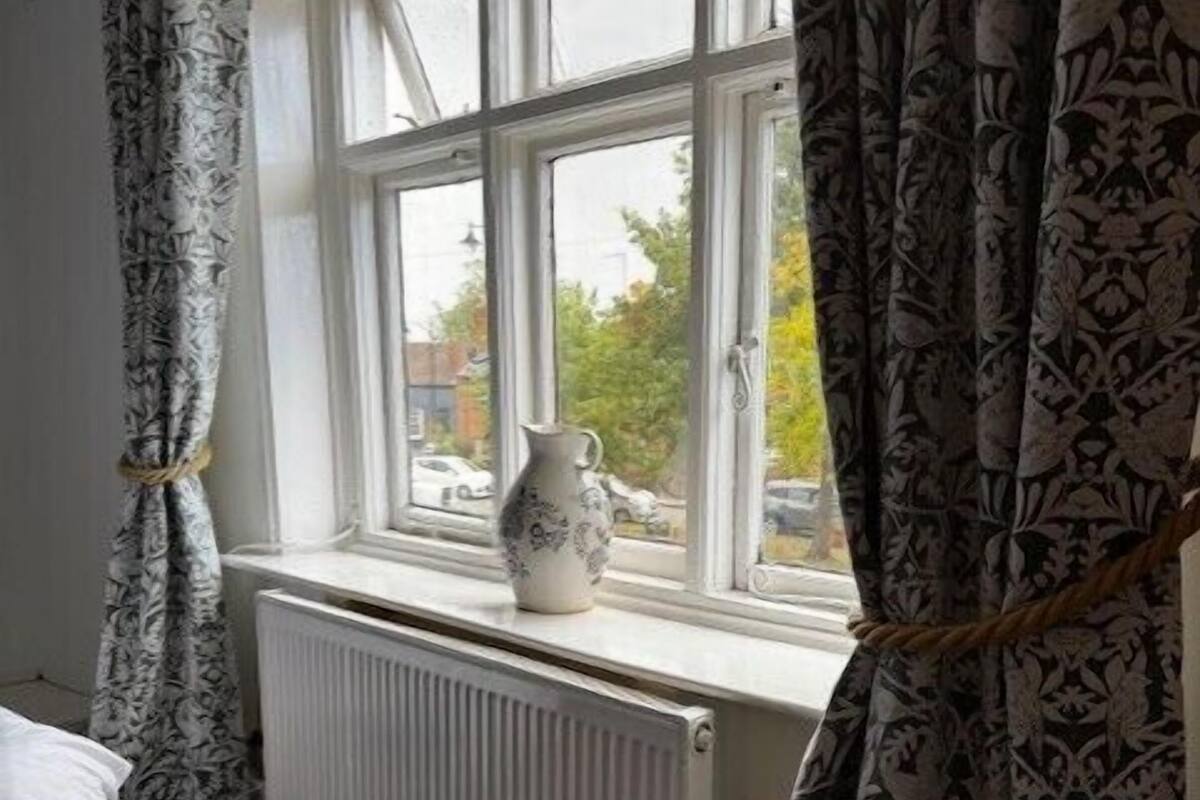Ein Schlafzimmer mit Fenster, Heizkörper und einer Vase auf der Fensterbank.