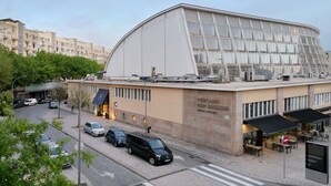 A modern building with a curved glass facade, a parking area, and a street view with cars and trees. - Hotel da Música (Porto)