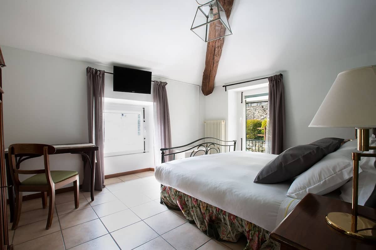 A bedroom with a bed, a desk, a chair, a TV, and a window with curtains.