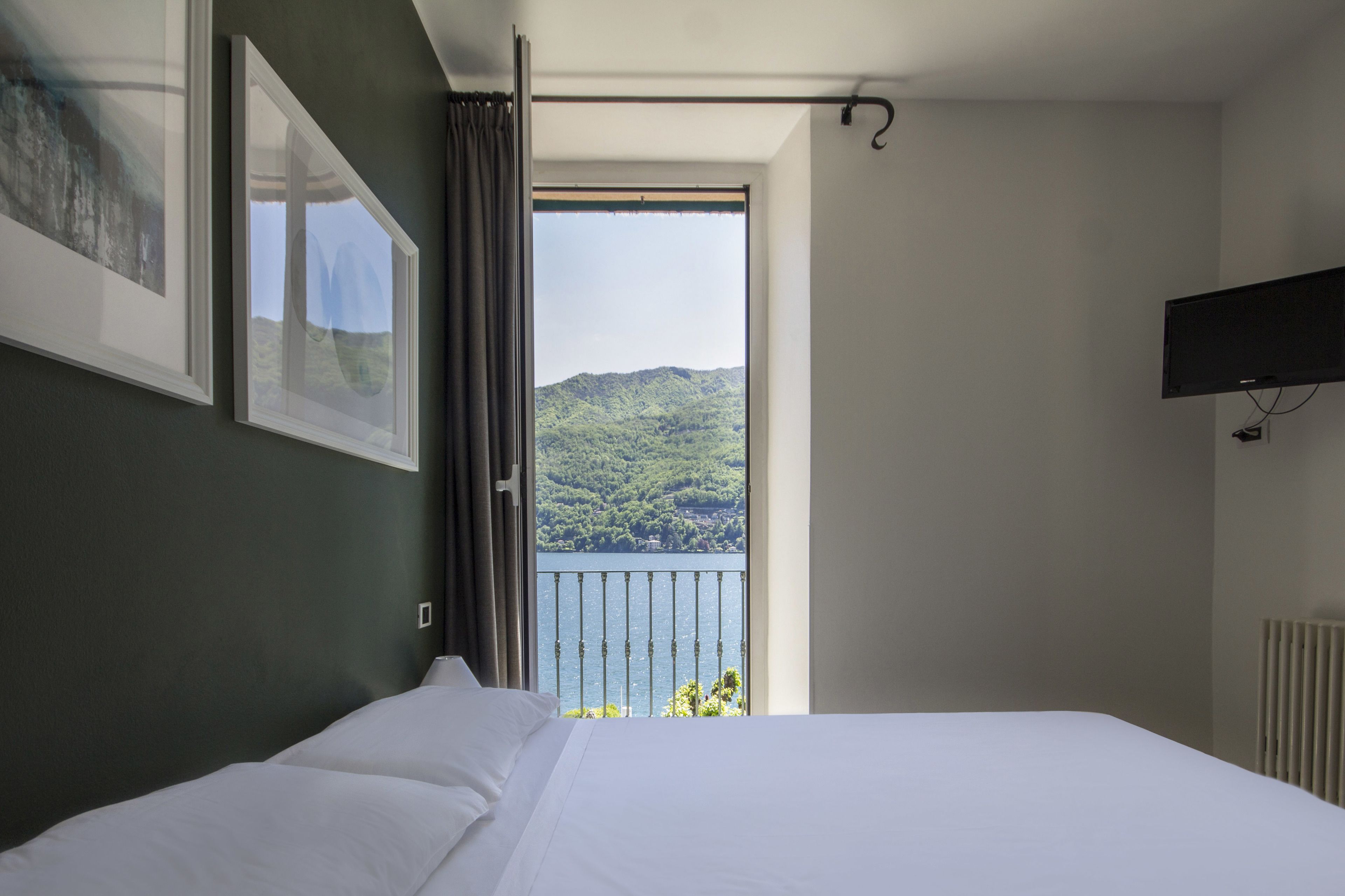 Quarto com cama, janela com vista para uma paisagem montanhosa, TV na parede e radiador.