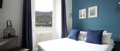 A bedroom with a bed, a window with a view of a mountain, a radiator, and a nightstand with a lamp.