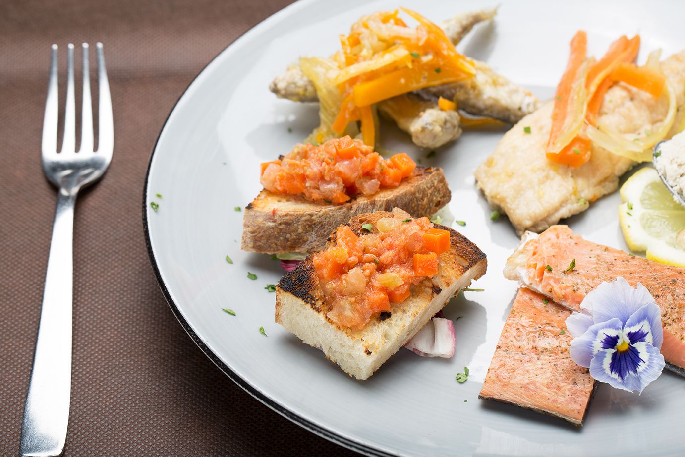 A plate with grilled salmon, avocado slices, and a small flower.