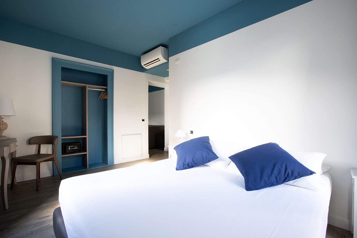 A bedroom with a bed, a chair, a desk, and a wardrobe.