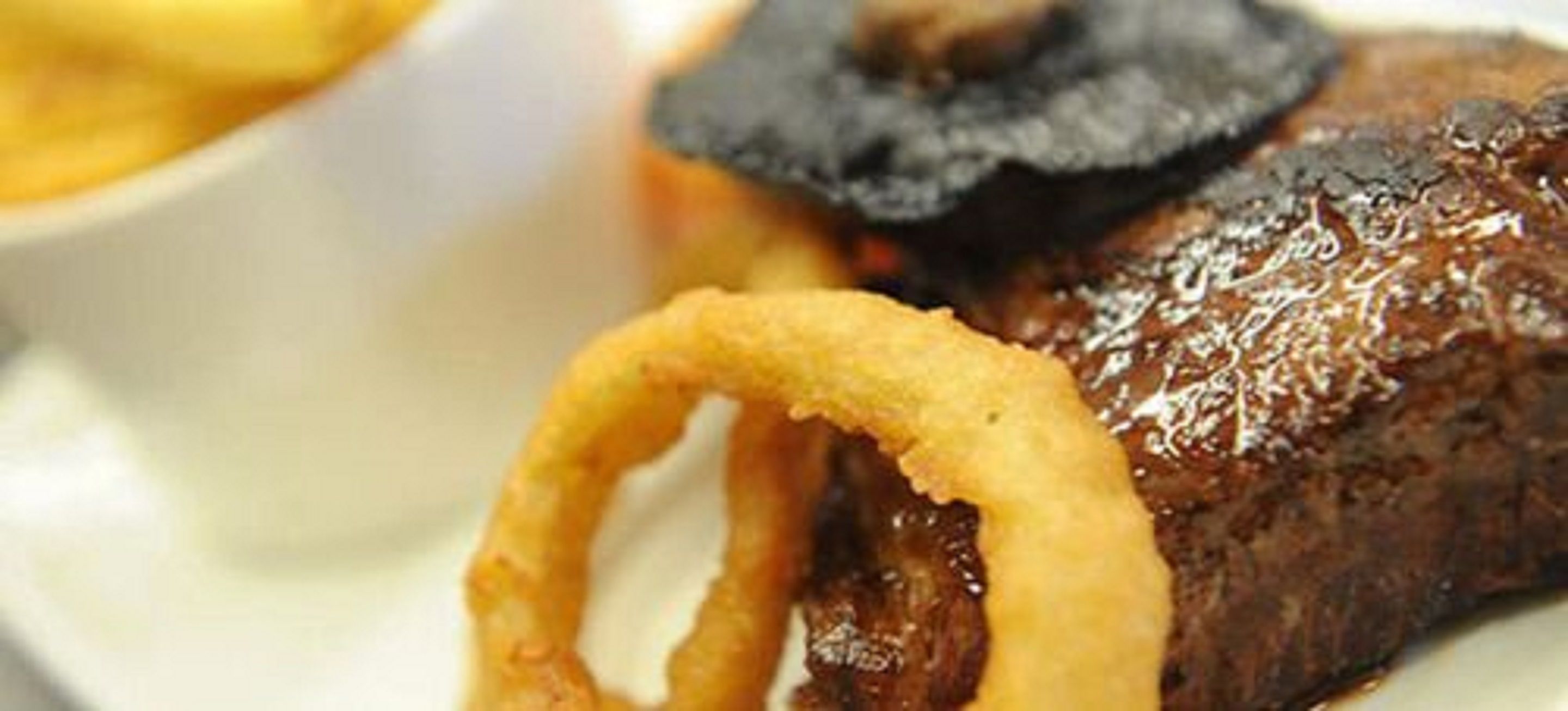 Une assiette avec un steak, des oignons frits et une sauce brune.