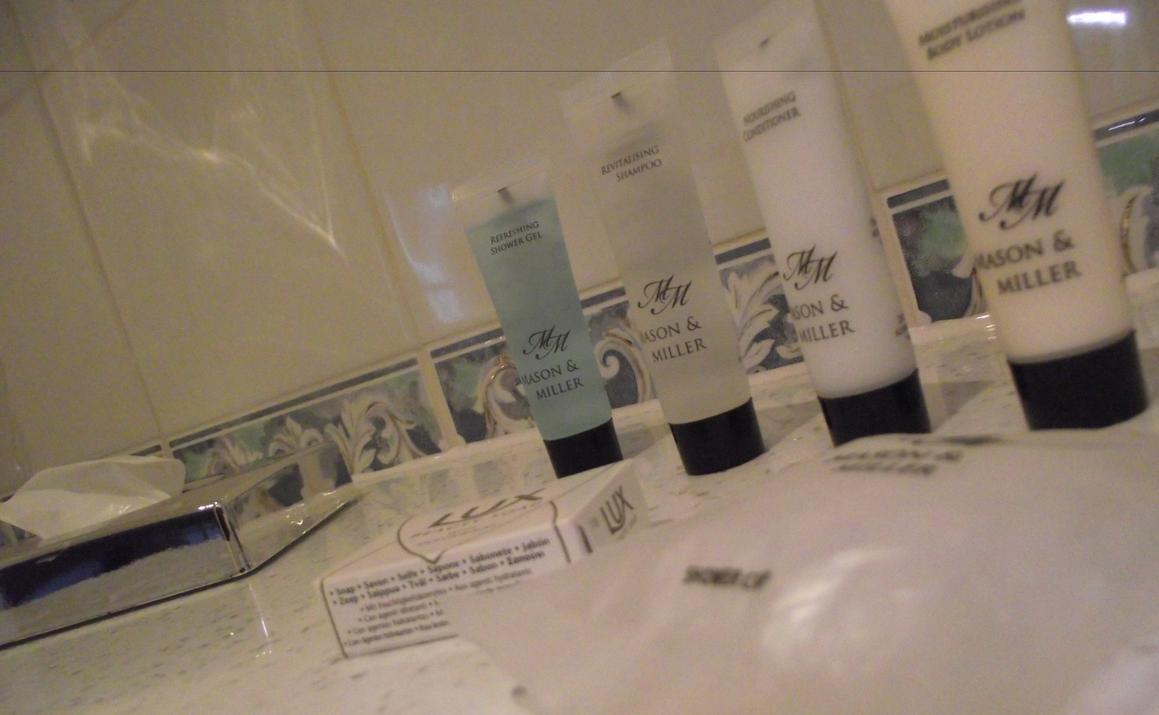 Une salle de bain équipée de produits de toilette, notamment un flacon de shampoing revitalisant, un flacon de gel douche Mison & Miller et un savon Lux.