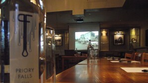 A conference room with a wooden table, a bottle labeled "PRIORY FALLS," and a projection screen in the background. - Sturdy's Castle Country Inn (Kidlington)