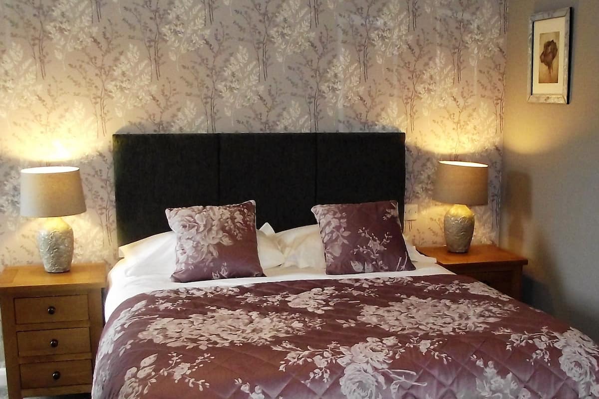 A neatly made bed with a floral bedspread, two bedside lamps, and a floral wallpapered wall.