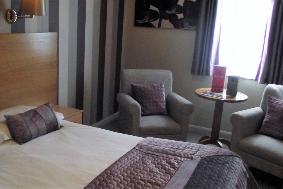 A hotel room with a bed, two armchairs, a small table, and a wall-mounted lamp.