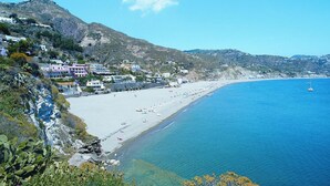 Una cittadina costiera con edifici sulla spiaggia, mare cristallino e una montagna sullo sfondo.
