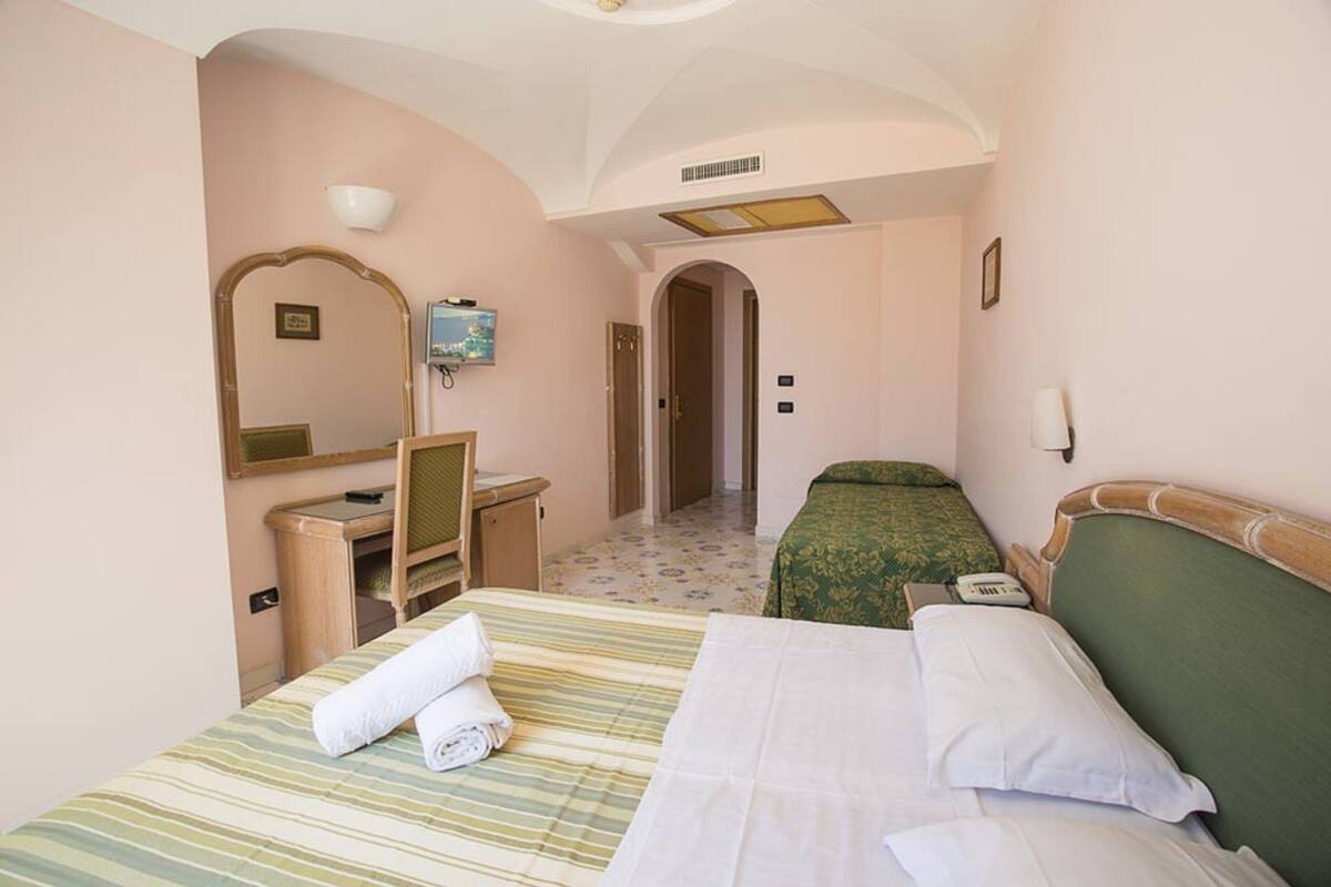 A hotel room with a bed, a desk, a chair, a mirror, and a television.