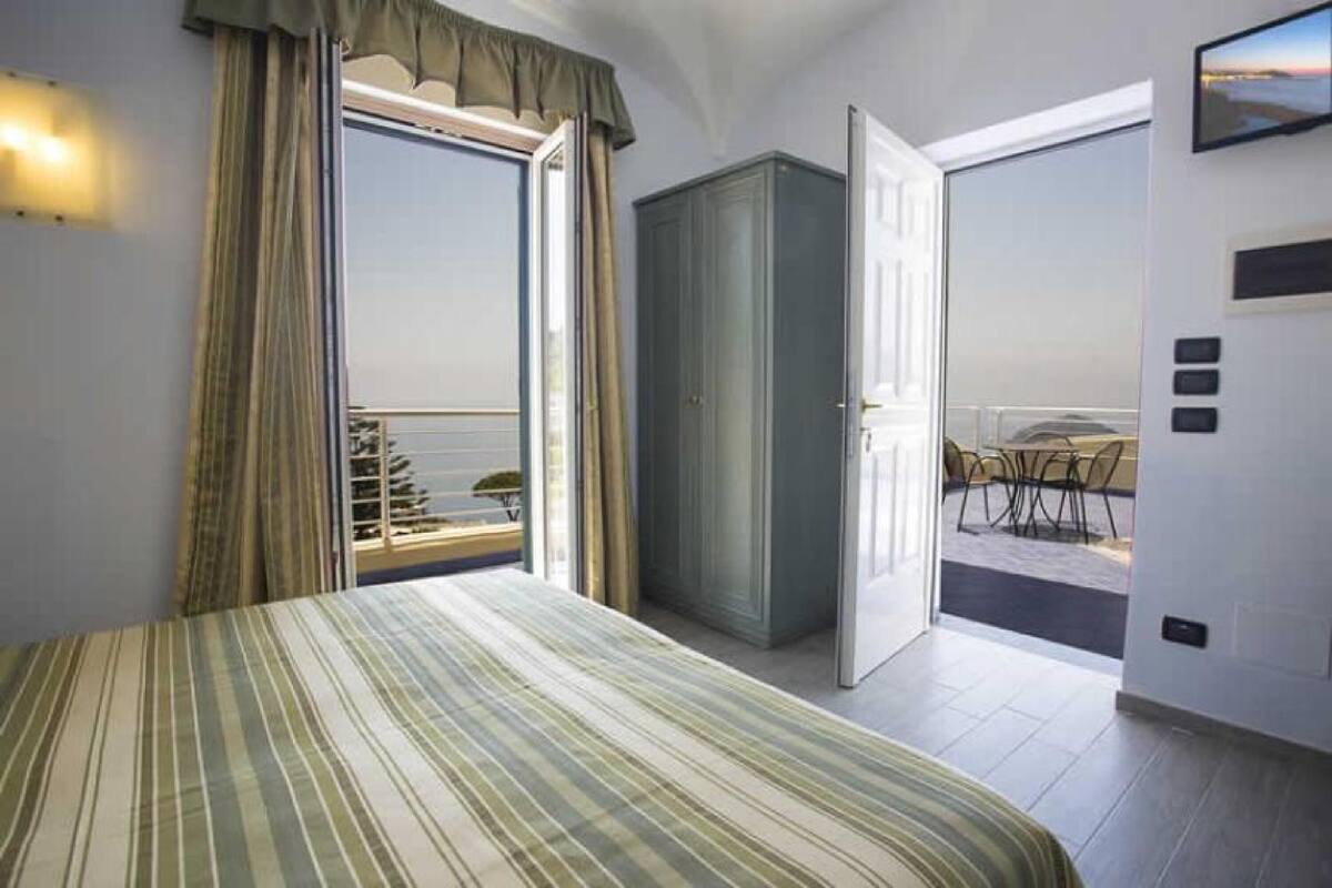 A bedroom with a bed, a wardrobe, and a balcony with a table and chairs.